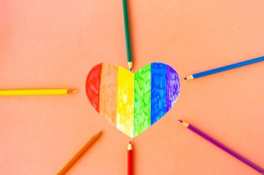 Pembe arka planda lgbtq renklerinde kalp ve renkli kalemler, üst görünüm