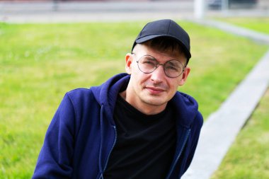 Şehir parkında gözlüklü ve şapkalı bir gencin portresi.