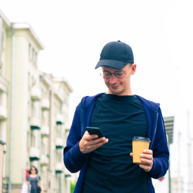 Delikanlı alt geçide inip elinde kahve ve telefon tutuyor.