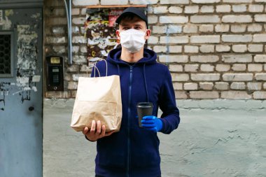 Koruyucu maskeli, elinde kese kâğıdıyla evin girişine yakın bir yere yemek getiren adam.