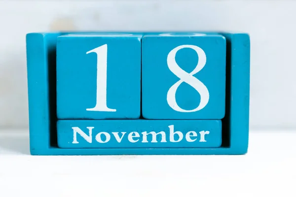 November 18. Blue cube calendar with month and date on wooden background.
