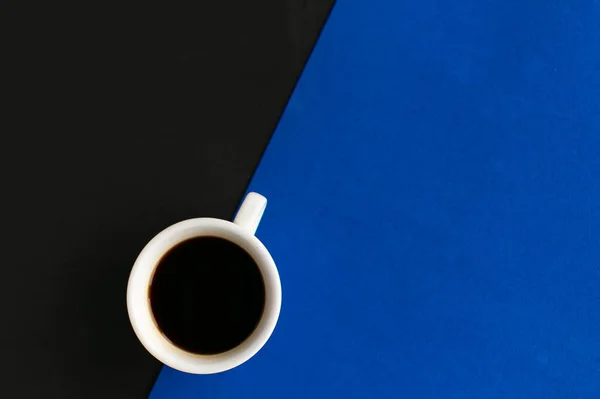 Coffee cup on geometric blue and black background, top view, copy space for the text, minimal concept
