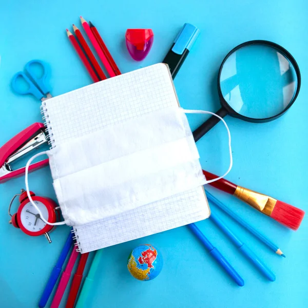 School supplies and medical mask on blue background, top view. Back to school concept