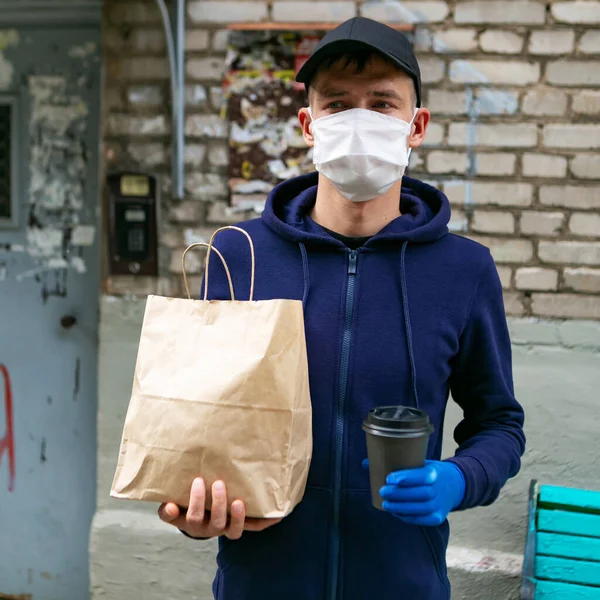 Food delivery man in protective mask with paper bag near the entrance of house, close up