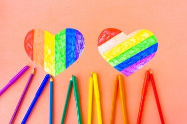 Lgbtq renklerinde iki kalp ve pembe arka planda renkli kalemler, üst görünüm