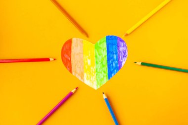 lgbtq renklerinde kalp ve parlak turuncu arka planda kalemler, üst görünüm
