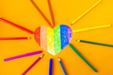 lgbtq renklerinde kalp ve parlak turuncu arka planda kalemler, üst görünüm