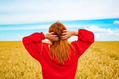 Buğday tarlasında genç bir kız, arkadan manzaralı.