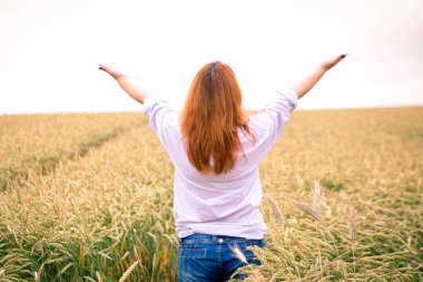 Buğday tarlasında genç bir kız, arkadan manzaralı.