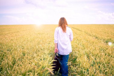 Kırsal yolda, buğday tarlasından geçen genç bir kadın.