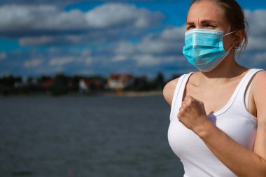 Tıbbi maske takan bir kadın, Coronavirüs salgını Covid-19. Spor, karantinada aktif yaşam. Corona Salgını 'nda atletizm pistinde açık hava koşusu.