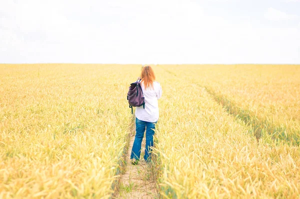 young woman in countryside road through wheat field, summer background