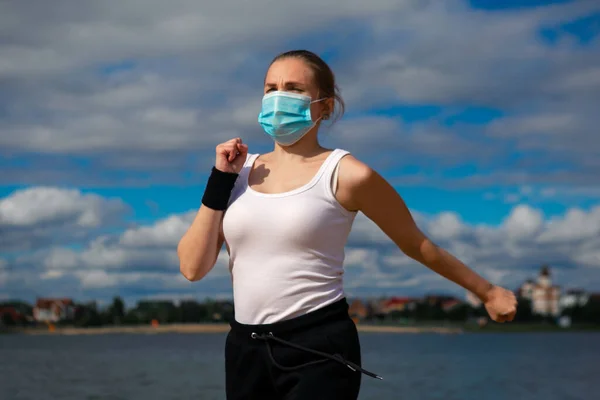 Woman wearing medical mask, Coronavirus pandemic Covid-19. Sport, Active life in quarantine. Outdoor run on athletics track in Corona Outbreak.