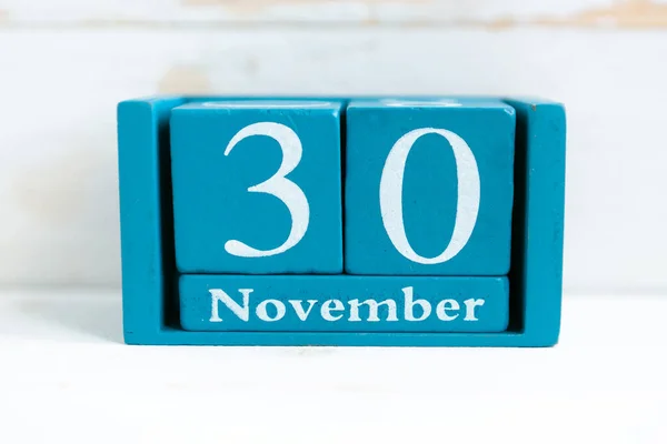 November 30. Blue cube calendar with month and date on wooden background.