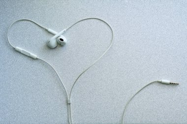 Beyaz kablolu kulaklıklar, gümüş arka planda kalp şeklinde kulaklık. Müzikal da