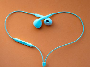 Beyaz kablolu kulaklıklar, turuncu arka plan üzerinde kalp şeklinde kulaklık. Müzik günü