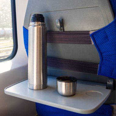 Trende katlanır masada kahve bardağı olan metal bir termos