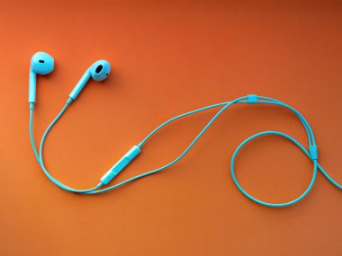 Beyaz kablolu kulaklıklar, turuncu arka planda kulaklık. Müzik günü