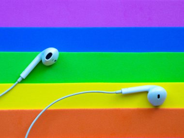 Beyaz kablolu kulaklıklar, çok renkli gökkuşağı arka plan (lgbt) kulaklık. Müzik günü