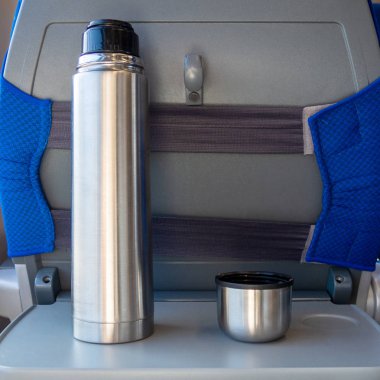 Trende katlanır masada kahve bardağı olan metal bir termos