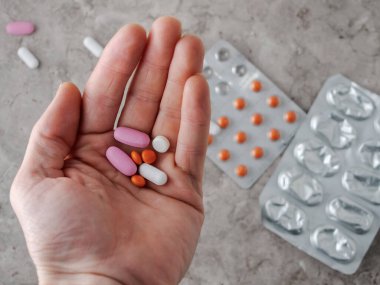 Adamın elinde bir sürü ilaç var, arka planda ilaç kutuları..