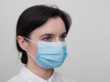 Korunabilir tıbbi maske takan genç Avrupalı bir kadının portresi. Caronavirus Cavid 19 ve insan karantinası kavramı. Beyaz duvarda maskeli bir kız. Maskeli sağlık görevlisi.