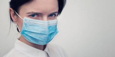 Korunabilir tıbbi maske takan genç Avrupalı bir kadının portresi. Caronavirus Cavid 19 ve insan karantinası kavramı. Beyaz duvarda maskeli bir kız. Maskeli sağlık görevlisi.