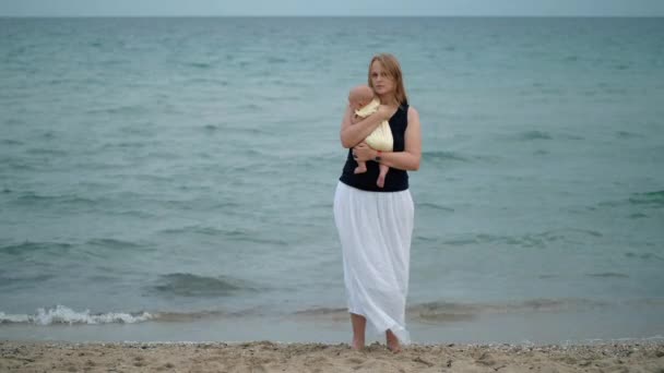 Madre abrazando al bebé, escena en la playa contra el mar — Vídeos de Stock