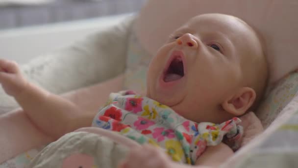 Baby flicka två månader liggande i bouncy säte och gäspningar — Stockvideo