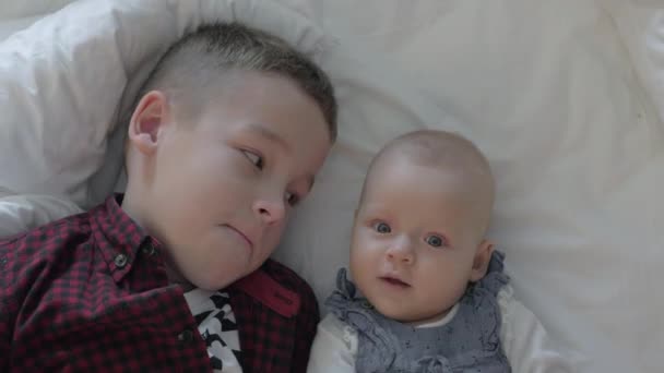 Мальчик и его младшая сестра лежат на кровати — стоковое видео