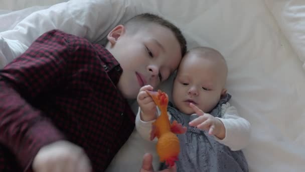 Hermano y hermana acostados en una cama y jugando — Vídeo de stock