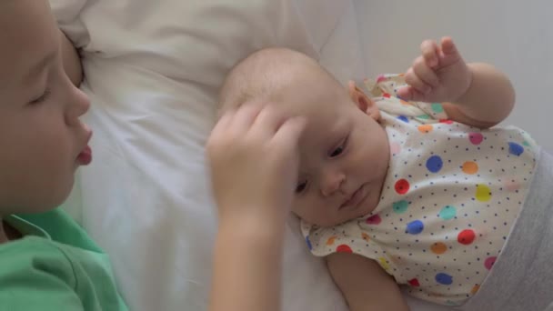 Niño acostado en una cama con su hermana pequeña y acariciando su cabeza — Vídeos de Stock