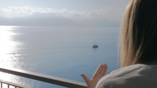 Женщина на балконе разговаривает с телефоном и с видом на море позади нее — стоковое видео