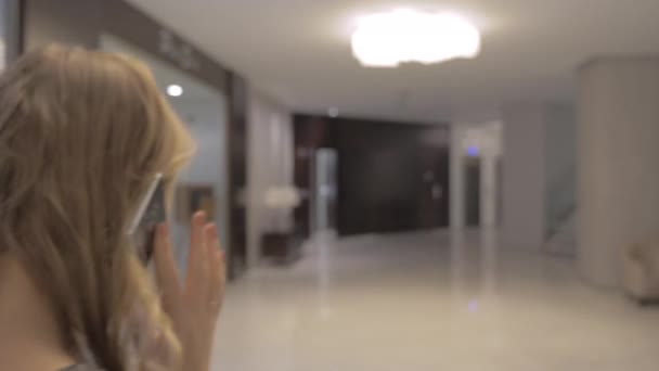 Jonge vrouw met telefoon praten wandelen in de hal van het hotel — Stockvideo