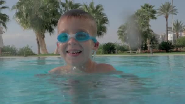 Веселый мальчик купается в бассейне на летних каникулах — стоковое видео