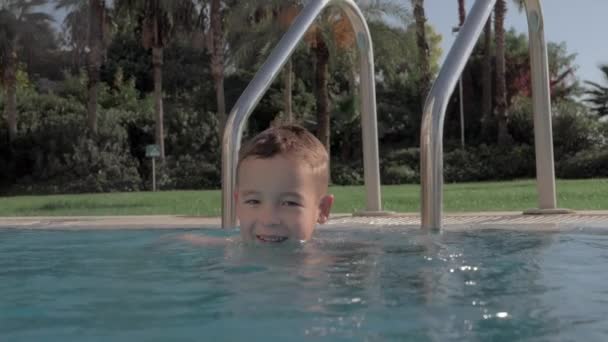 Alegre niño salpicando agua en la piscina — Vídeo de stock