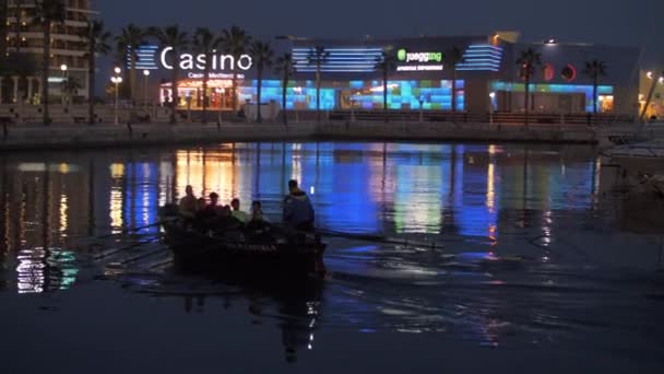 Vista notturna del lungomare della città e della barca a remi nel porto — Video Stock