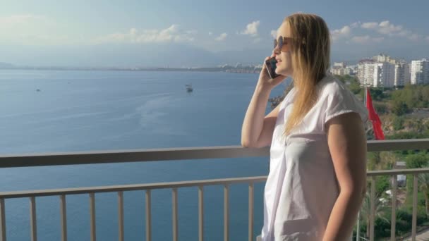 Mujer hablando por teléfono y disfrutando de la vista al mar desde el balcón — Vídeos de Stock