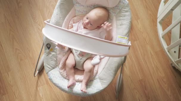 彼女は彼女の赤ちゃん椅子を見て周りに座っている間 顔を作る新生児女の子のミディアム ショット — ストック動画