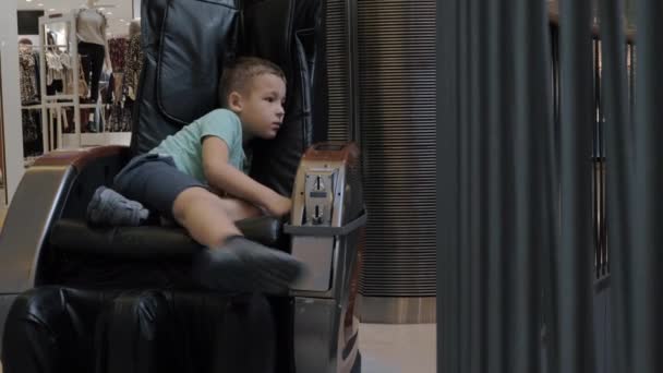 Un chico aburrido en una silla de masaje en el centro comercial — Vídeo de stock