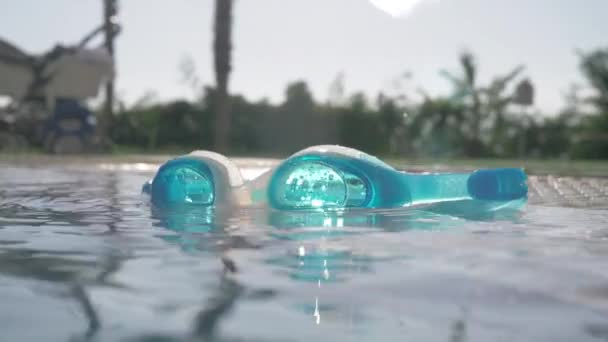 Eine Nahaufnahme einer blauen Brille auf einer offenen Poolfläche an einem sonnigen Tag — Stockvideo