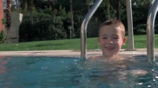 Um menino em uma piscina aberta feliz salpicando a água — Vídeo de Stock