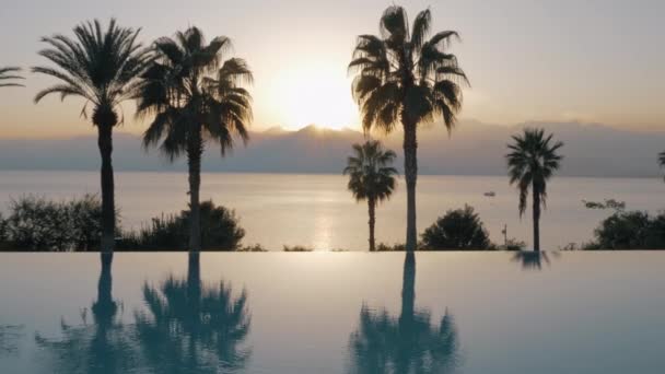 Un plan steadicam d'une piscine ouverte et le coucher du soleil par la mer derrière elle — Video