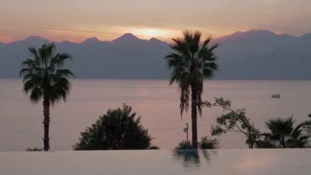 Ein offenes Schwimmbad und ein abendlicher Blick auf das Meer vor den Bergen — Stockvideo