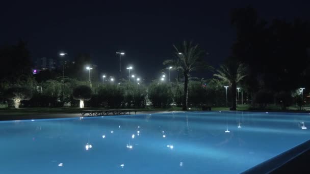Una toma steadicam de una piscina abierta iluminada por la noche — Vídeo de stock