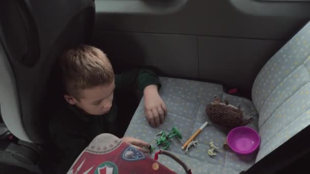 A boy sitting on a cars floor playing with some toys on a back seat — Stock Video