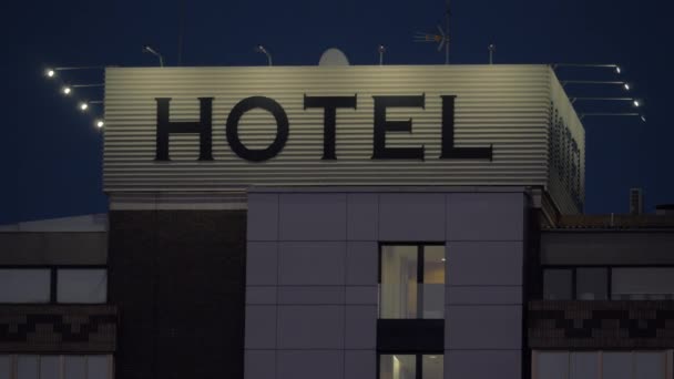 Un panneau d'hôtel sur un toit d'un bâtiment contre le ciel sombre du soir — Video