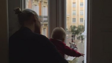 Bir kız çocuğu annesi onun oturma odasında evde bir şehir daire ile pencereden dışarı bakarak, orta vurdu