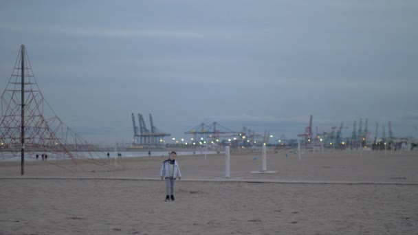 Ung pojke promenerar på stranden på en kall dag — Stockvideo