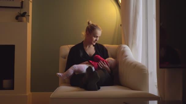 ウィンドウと母乳育児 ヶ月の娘がソファに座っている女性 膝の上持株子を母し キスを終えた後 — ストック動画